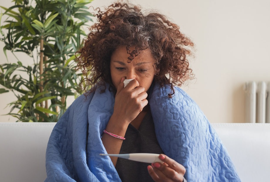 woman with the flu with blanket, tissue, thermometer