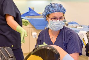 A doctor performing surgery wearing a mask, glasses, scrubs, a facemask and hair cap. 