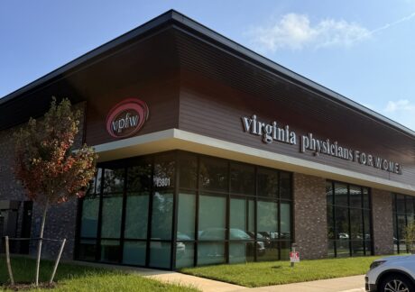 Exterior of the corner of VPFW St. Francis building with pink oval vpfw logo sign and virginia physicians for women sign. Brown siding, brown brick, and large windows.