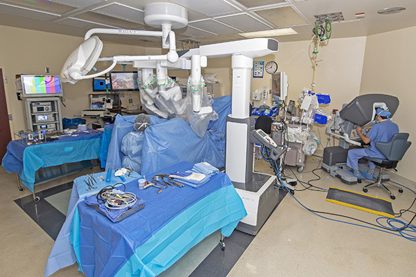 VPFW's Dr. Ramzi Aboujaoude wearing blue scrubs with head looking down into a screen and hands moving robotic machinery doing surgery at Johnston Willis hospital