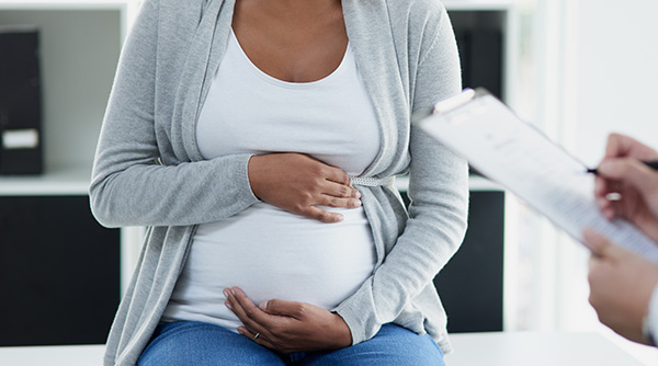 pregnant woman holding stomach on table while doctor holds clipboard