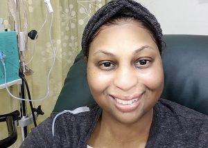 Woman smiling in a cancer treatment center chair with medical cords hanging next to her