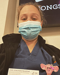 Dr. Dogal wearing scrubs and a mask and holding her COVID-19 vaccination record card