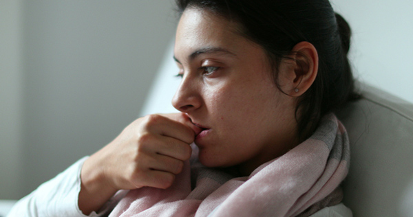 A woman who struggles with anxiety related to hormones bites her nails looking pensive.