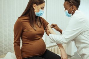 Pregnant brunette in brown shirt getting COVID-19 vaccine recommended for pregnant women