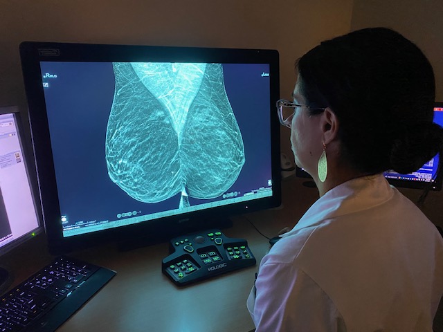 Dr. Nicole Kelleher in a while lab coat reading a 3D mammogram on a computer screen in the dark