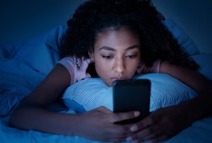 Woman whose hormones affect her sleep looking at her phone in bed