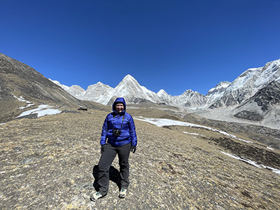 Dr. Draper hiking in Nepal with blue sky and white mountains in background 
