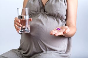 Pregnant woman holding a prenatal vitamin wondering when to start taking a prenatal vitamin