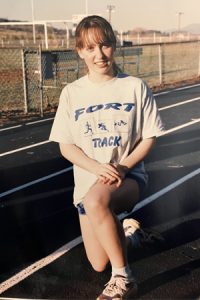 Dr. Jennie Draper's track team photo from middle school, smiling and kneeling on the track
