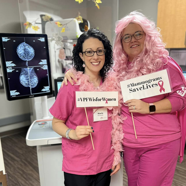 Mammography techs promoting free mammograms for uninsured women, wearing pink and posing by the mammography machine