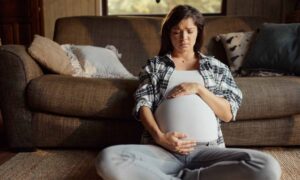 A pregnant woman holds her belly, looking concerned