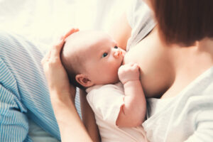 A mother in striped pants breastfeeds a young baby holding her breast
