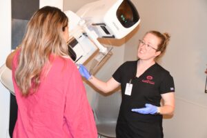 Mammography Tech in black scrubs with pink VPFW logo guiding a patient through her mammogram