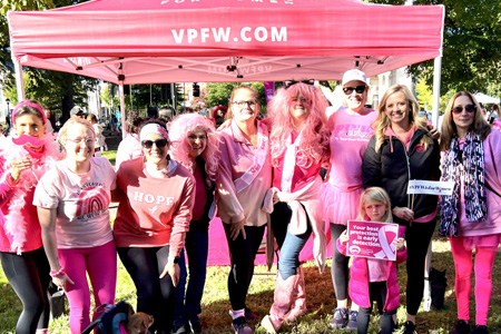 Team of women and one little girl, all wearing pink in front of pink VPFW tent in a grassy park