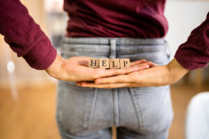 Woman secretly holds scrabble tiles behind her back that spell out "HELP"