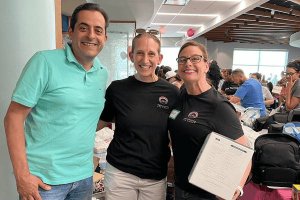 A man and two woman, arms around eachother and smiling, in a busy, messy lobby of an OB/GYN practice