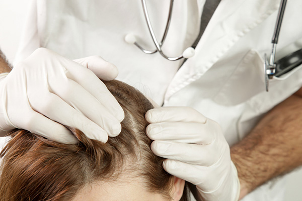 A physician examines a woman’s scalp during a well woman exam