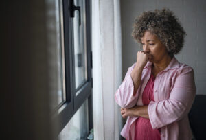 A concerned older woman gazes out the window, deep in thought. 