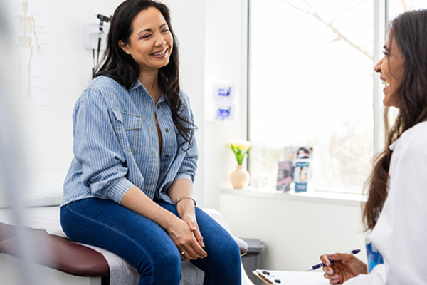gynecology patient smiling while sitting on exam table talking to gynecologist