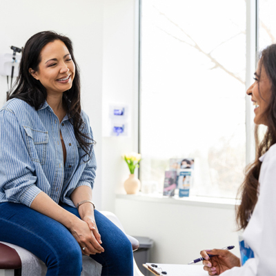 gynecology patient smiling while sitting on exam table talking to gynecologist