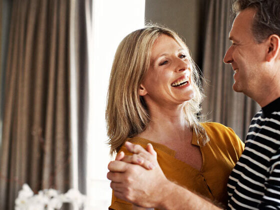 Middle aged couple smiling while dancing in a bedroom