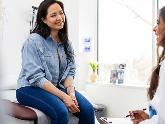 gynecology patient smiling while sitting on exam table talking to gynecologist