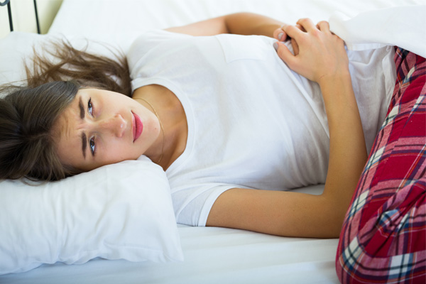 A teen girl with cramps lays on her bed.